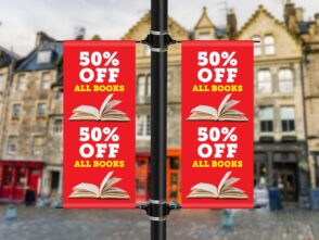 Double-sided lamp post banners displaying "50% OFF ALL BOOKS" with an open book graphic, promoting a sale in an urban setting.