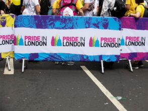 Crowd barrier displaying "Pride in London" branding, vibrant colours, and festive atmosphere at a public event.