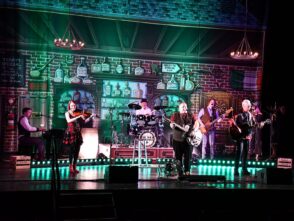 Musicians performing on stage with a vibrant pub-themed backdrop, featuring a bar and various bottles, highlighting the importance of custom stage backdrops for events.